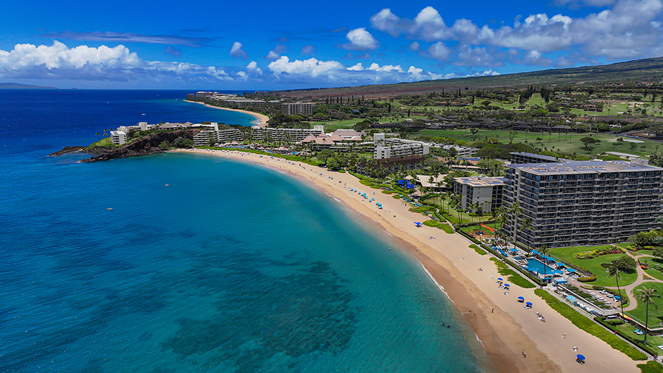 Aerial view of Kāʻanapali Beach and the West Maui Mountains under clear skies.