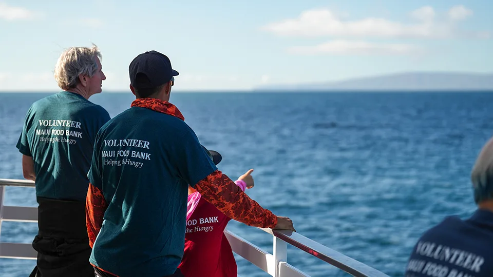 Maui Food Bank volunteers looking out over ocean during appreciation cruise with West Maui mountains visible