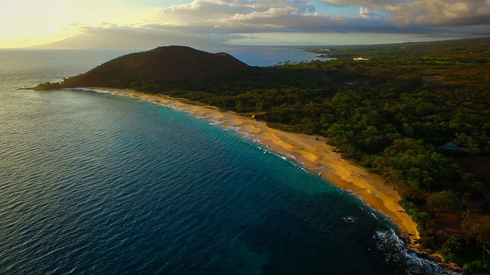 Aerial view of Big Beach in Mākena State Park, showing golden sand and turquoise waters backed by green hills.
