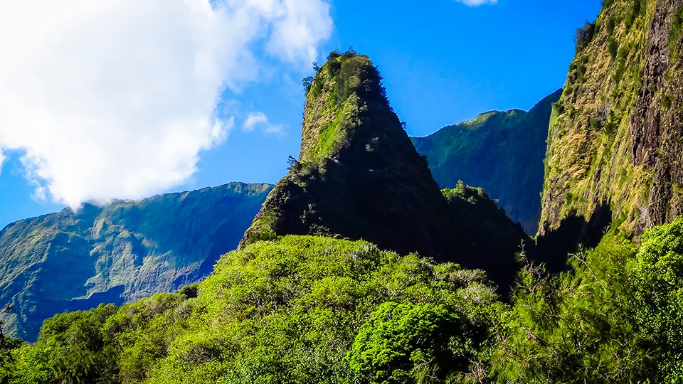 Iconic ʻĪao Needle rising from lush greenery under a blue sky.