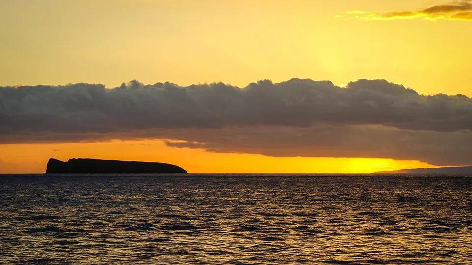 Golden sunset at Poʻolenalena Beach casting warm light across calm ocean waters.