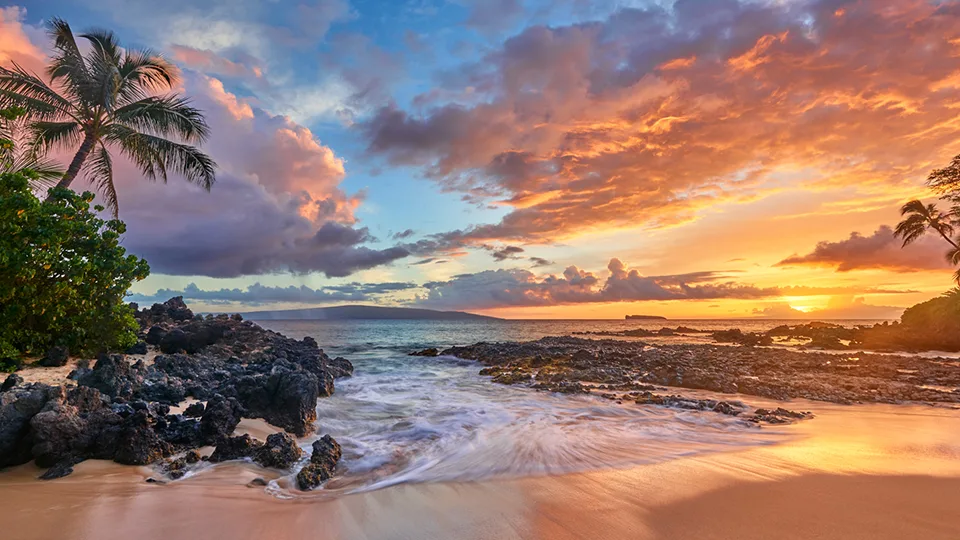 Colorful sunset over Makena Cove with lava rocks and golden sand reflecting the evening light.