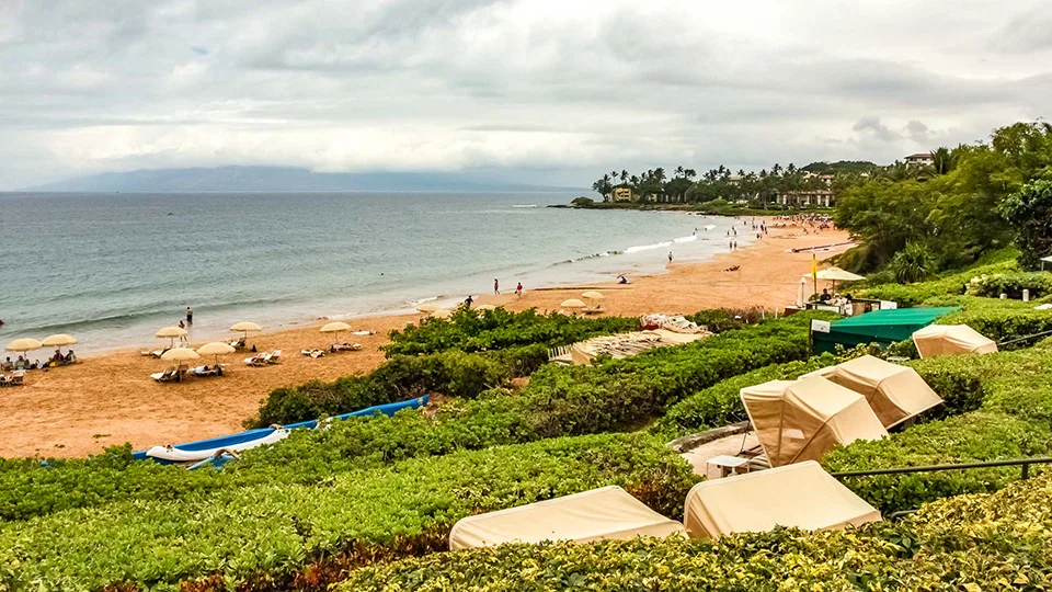 Overcast morning view of Wailea Beach lined with lounge umbrellas.