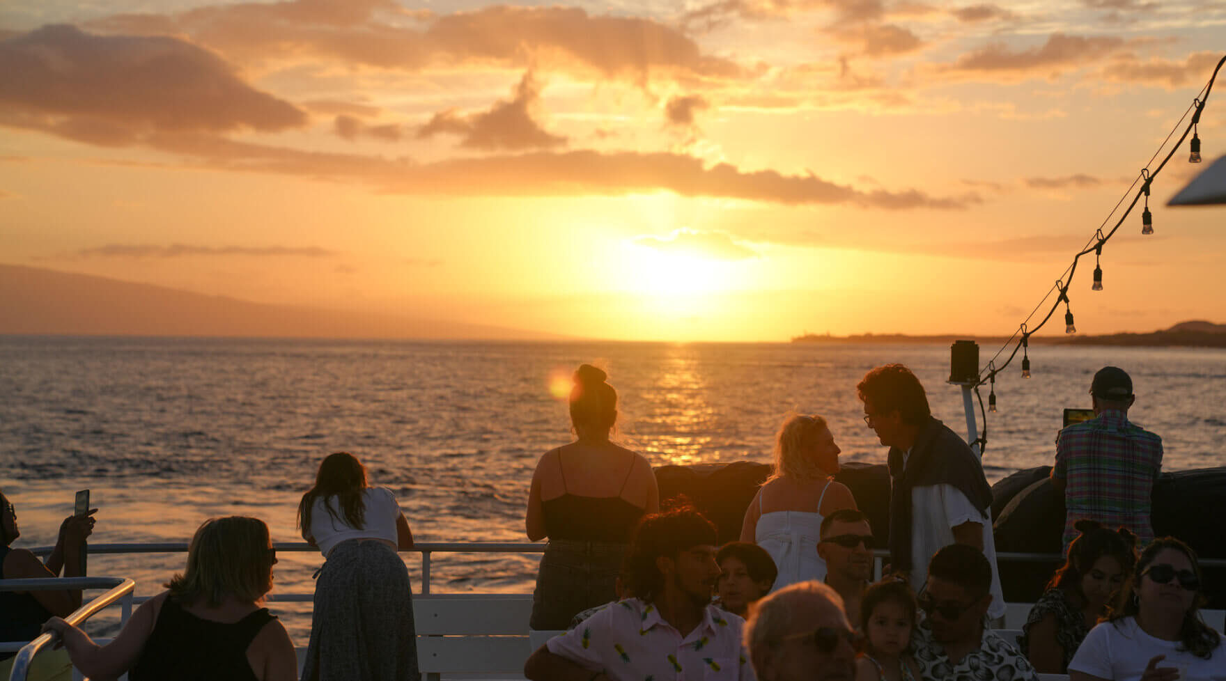 Guests watching the sunset from the open deck of the Pride of Maui catamaran