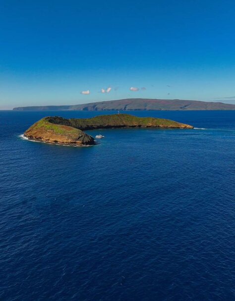 Molokini Crater with Maui in the distance on a calm morning.